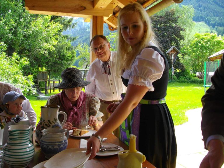 Семья наслаждается пирогом и напитками за деревянным столом на ферме Schloss Saalhof в зелени