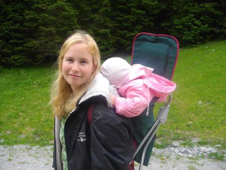 Молодая женщина несет спящего ребенка в рюкзаке во время семейного отдыха на природе недалеко от Целль-ам-Зе