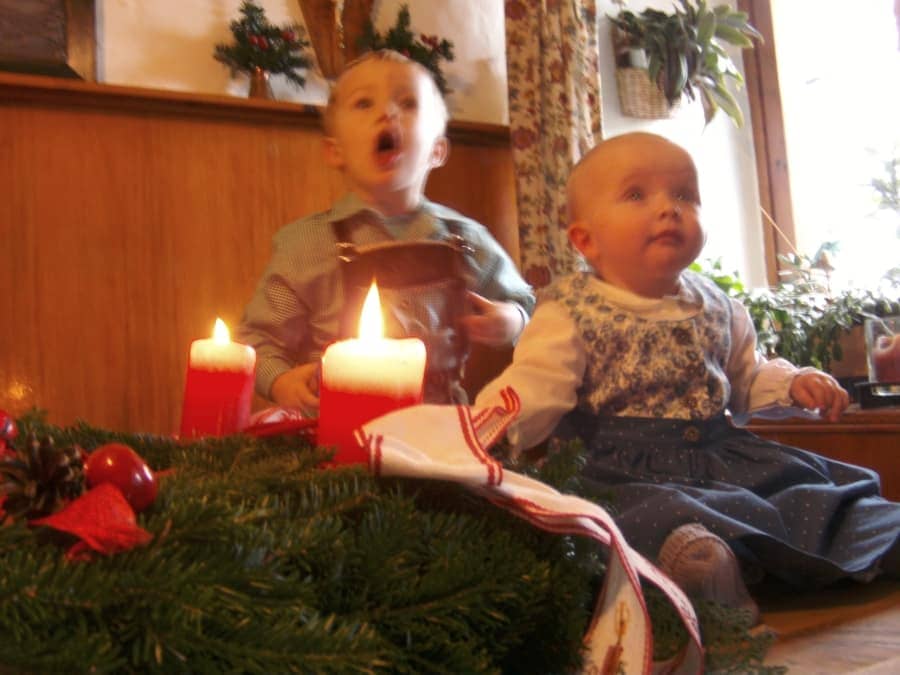 Zwei Kinder in Tracht neben Adventskranz mit Kerzen, gemütliche Bauernhofatmosphäre im Schloss