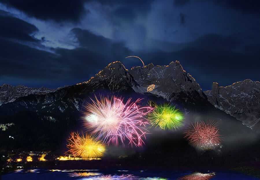Buntes Feuerwerk über nächtlicher Berglandschaft bei Zell am See, gespiegelt im See