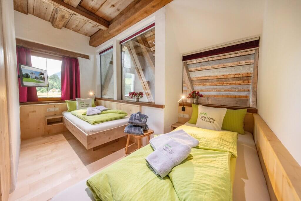 Helles Schlafzimmer im Schloss Saalhof mit zwei Einzelbetten, Holzdecke und TV, Familienurlaub