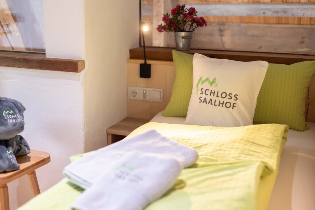 Modernes, gemütliches Bett im Schloss Saalhof mit Logo-Kissen, Handtüchern und Blumen, Bauernhofurlaub