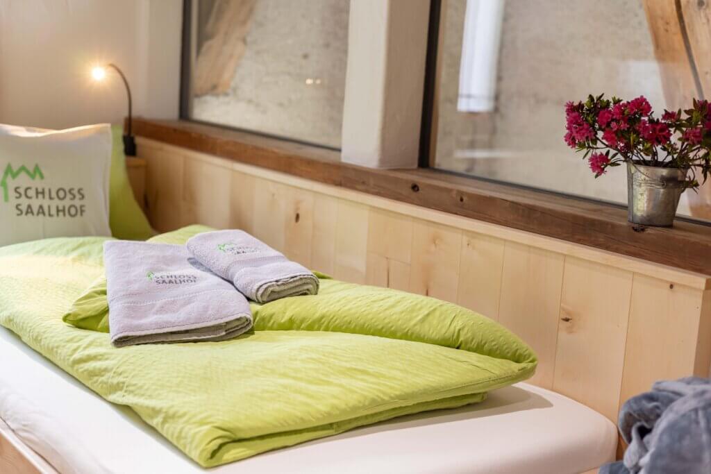 Gemütliches Bett mit Schloss Saalhof-Logo, Handtüchern und Blumen im Appartement Zell am See