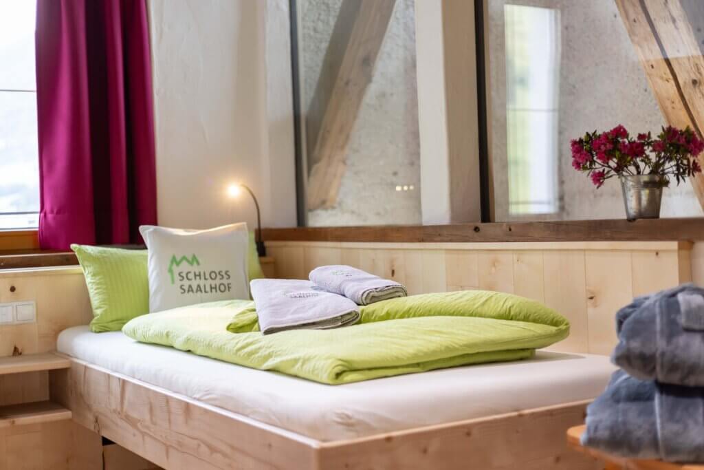 Gemütliches Bett im Schloss Saalhof Appartement mit grüner Bettwäsche, Handtüchern und Blütenvasen